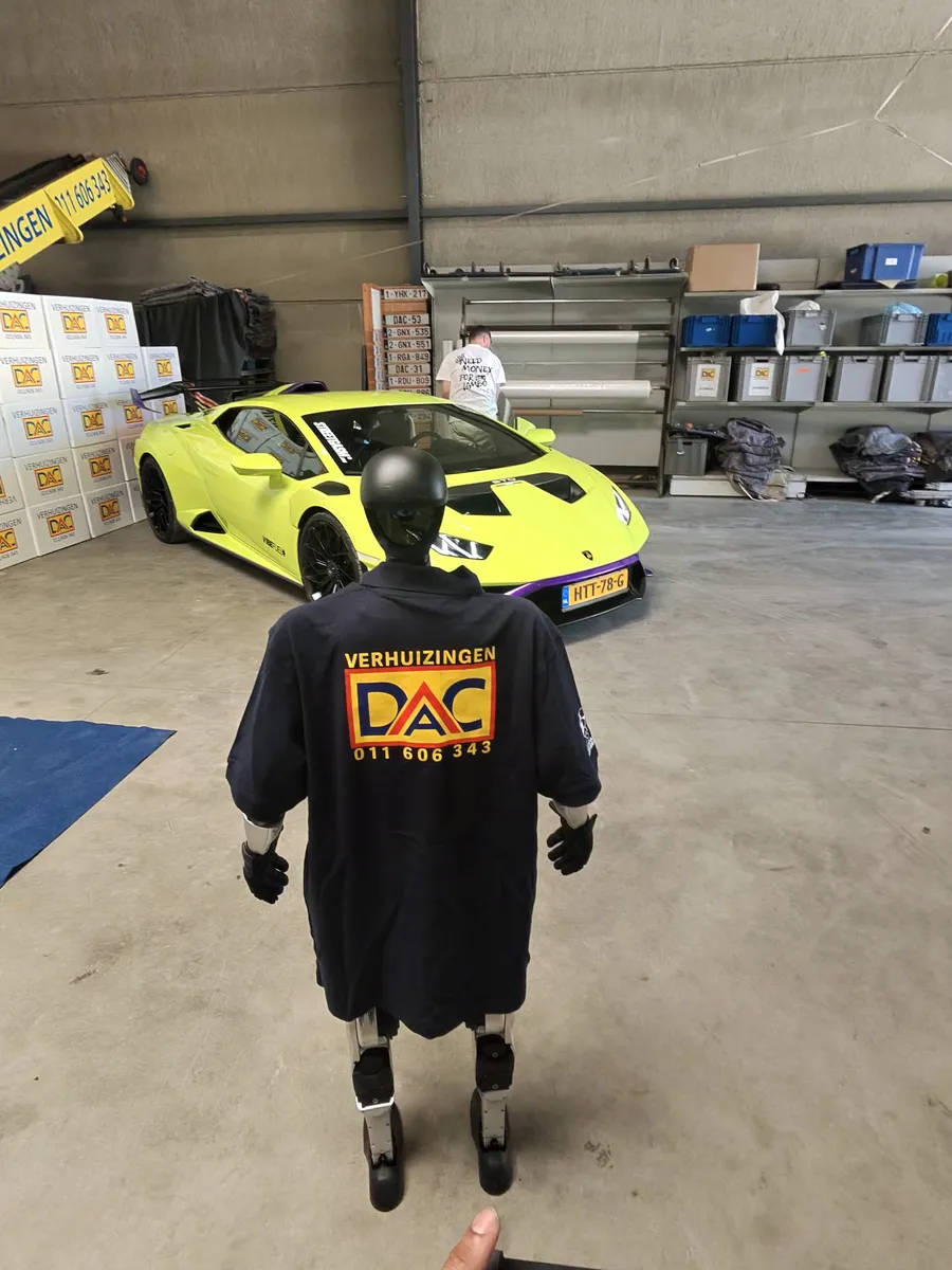 RELMO in een DAC Verhuizingen-shirt naast een sportwagen in een loods